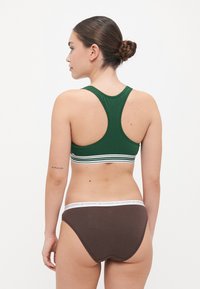 Πράσινο αμάνικο μπλουζάκι με λευκές και πράσινες ρίγες στο κάτω μέρος, συνδυασμένο με καφέ σλιπ με λευκή ζώνη. Απαλή, ελαφριά ύφανση.