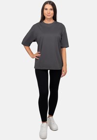 Grijze oversized T-shirt van katoen, met korte mouwen en een ronde hals, gecombineerd met zwarte legging en witte sneakers.