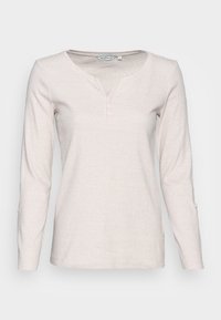 Beige Langarmoberteil mit Henley-Ausschnitt, ausgestattet mit drei Knöpfen, gerippter Textur und seitlichen Schlitzen am Saum. Aus weichem Baumwollgemisch.