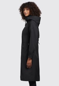 Cappotto lungo impermeabile nero con cappuccio, vita con cordino e cerniere laterali. Presenta una superficie liscia e polsini con bottoni.