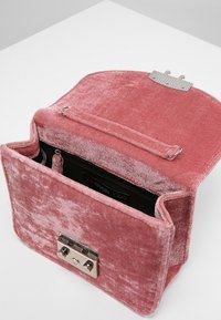 Borsa a tracolla in velluto rosa con una texture morbida, forma rettangolare, chiusura superiore a battente e tasca interna con zip. Presenta dettagli cuciti.