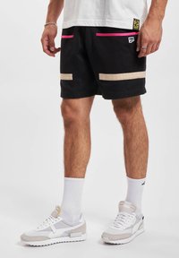 Schwarze Shorts mit pinken und beigen Akzenten, ausgestattet mit Netz-Taschen und einem Logo-Tag. Kombiniert mit weißen Sneakers und gerippten weißen Socken.