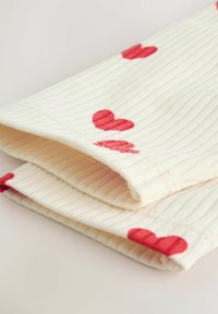 Puuvillane kangas soonilise tekstuuriga, kreemikas toon punaste südamekujudega, servadelt kokku volditud, näidates korralikku õmblemist.