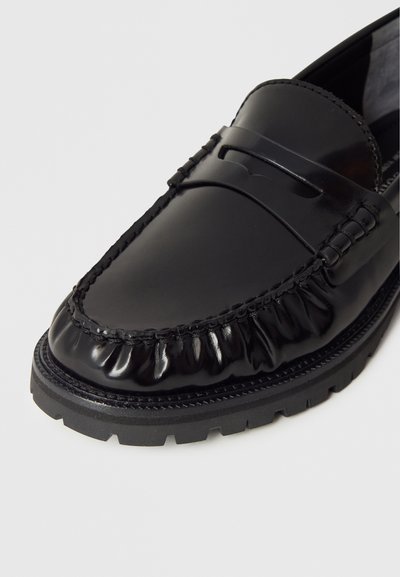 Czarny skórzany mokasyn o błyszczącym wykończeniu, z rowkowanym przeszyciem na cholewce, gumową podeszwą z fakturowanym wzorem oraz ozdobnym paskiem z przodu.