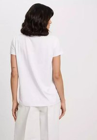 Biała koszulka z krótkim rękawem, z okrągłym dekoltem. Wykonana z miękkiej bawełny, o luźnym kroju, noszona na jasnych spodniach.