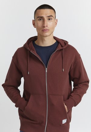 Maroon zip-up hoodie made of cotton blend, featuring a front zipper, adjustable hood, and front pockets. Minimalistic design with logo patch.