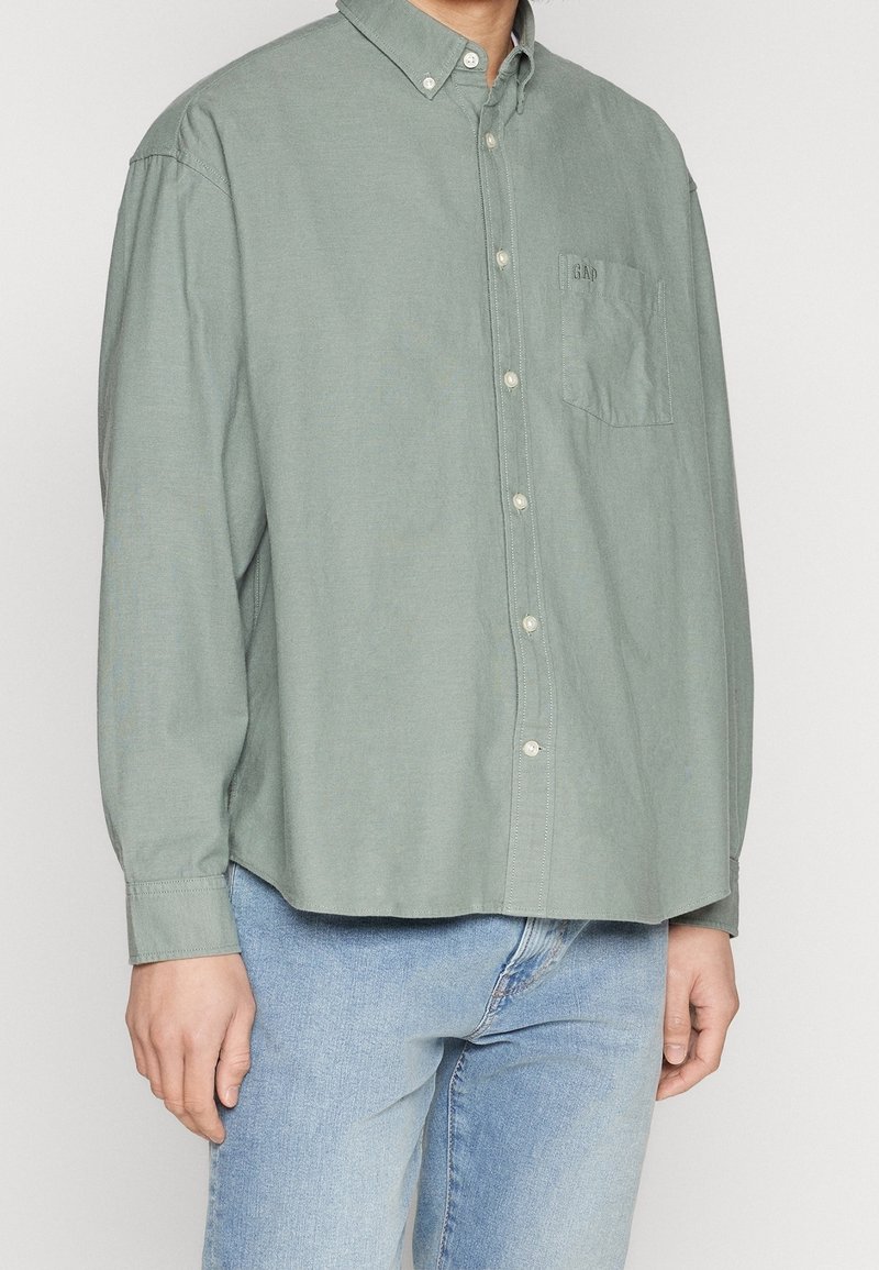 Chemise vert clair à boutons, avec une poche poitrine unique, un col et une fermeture à boutons, fabriquée en tissu doux avec une coupe décontractée.