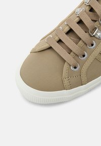 Baskets en toile beige avec design à lacets, œillets métalliques et semelle en caoutchouc blanche ; présentent une texture lisse et une forme profilée basse.