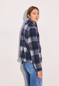 Paarse en groene geblokte fleecejas met een staande kraag, met een cropped ontwerp en een voorzak. Gecombineerd met lichtblauwe denim jeans.