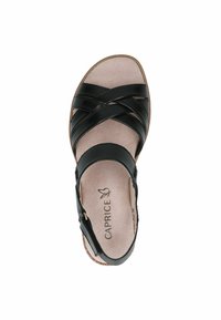 Sándalo de cuero negro con tiras cruzadas, punta abierta y una plantilla beige suave. Correa ajustable en el tobillo con detalle de hebilla metálica.