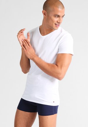 T-shirt bianco in cotone con scollo a V abbinato a shorts fitted blu navy. Il tessuto appare liscio, con un piccolo logo del marchio vicino all'orlo.
