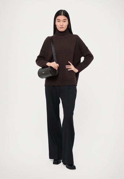 Pull en maille marron foncé avec un col montant, associé à un pantalon noir à jambe large. Un sac à main cylindrique noir avec une finition texturée et une sangle.