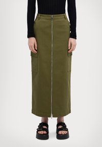 Gonna cargo lunga verde oliva con zip frontale, tasche laterali e siluetta dritta. Indossata con sandali neri con zeppa.