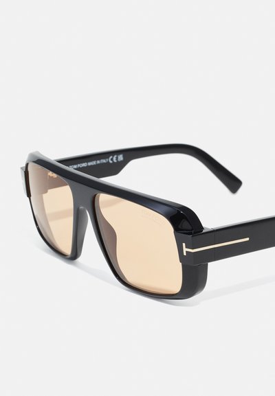 Gafas de sol negras rectangulares con lentes marrón degradado. Presentan un marco brillante, patas planas y un acento dorado en las bisagras.