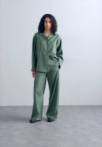 Set di abbigliamento da casa in seta verde composto da una camicia a maniche lunghe con bottoni e pantaloni a gamba larga, entrambi con una texture liscia e una vestibilità comoda.