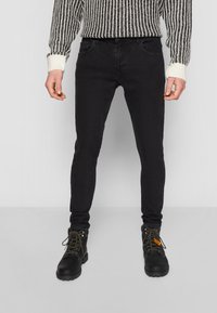 Musta skinny-farkut, valmistettu denimmateriaalista, joissa on viisi taskua ja yksinkertainen muotoilu, yhdistettynä mustiin nauhakenkiin.