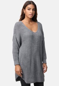 Szary, oversize sweter dzianinowy z głębokim dekoltem w kształcie V, prążkowanymi długimi rękawami i teksturowaną powierzchnią. Brzeg jest dłuższy po bokach.