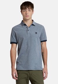Miestenská polo košeľa v melírovanej šedej farbe, zmes bavlny, s klasickým golierom, trojzakladovým zapínaním a námorníckymi manžetami. Logo Timberland na hrudi.