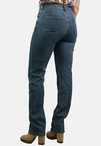 Jeans de mezclilla azul con una cintura de media altura, diseño de pierna recta y dos bolsillos traseros, combinados con tacones plataforma color marrón.