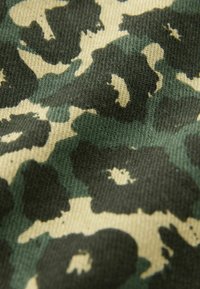 Tissu camouflage avec des motifs vert foncé et noir sur fond beige. Texture douce avec un design tissé.