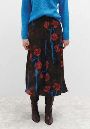 Ein brauner Blumenrock mit roten Blumen und blauen Stielen. Kombiniert mit einem blauen Strickpullover und knielangen bordeauxfarbenen Stiefeln, die einen geschichteten Look erzeugen.