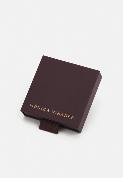 Caja de joyería cuadrada de color púrpura oscuro con acabado texturizado, que presenta un logo dorado "MONICA VINADER" en la parte frontal y una lengüeta de tirón marrón.