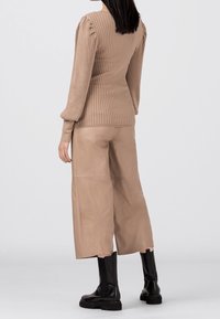 Pull beige côtelé avec épaules bouffantes, associé à un pantalon large en cuir beige et des bottines noires. Texture lisse, coupe ajustée.