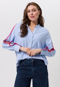 Blau-weiß gestreiftes Hemd mit Knopfleiste und roten Rüschendetails an den Ärmeln, mit Stehkragen und legerer Passform.