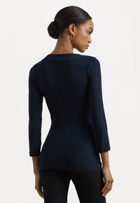 Navy blue, long-sleeve top in a fitted design with a scoop neckline. Smooth texture and subtle stitching detail at the shoulders.