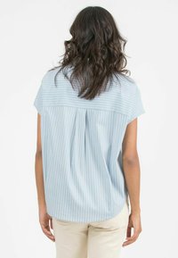 Blusa azzurra a maniche corte con strisce verticali bianche, caratterizzata da un dettaglio arricciato sulla schiena. Tessuto morbido con una vestibilità comoda.