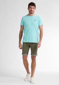 T-shirt en coton bleu clair à manches courtes et col rond, associé à un short vert olive retroussé au bas et des chaussures blanches.