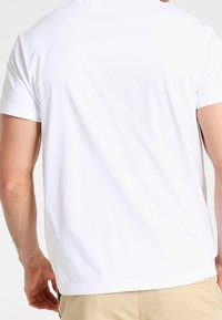 Vit bomullströja, korta ärmar, avslappnad passform. Lätt textur med rund halsringning och sytt nederkant. Vy från baksidan.