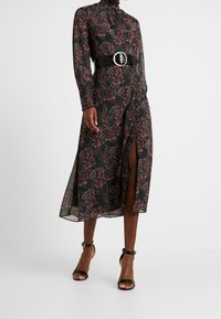 Pitkähihainen mekko, jossa on korkea kaulus, musta kangas, jossa on burgundin ja vihreän värisiä kukkakuoseja, sekä reiden korkeudelle ulottuva halkio. Mukana on leveä musta vyö.