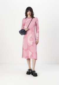 Rochie roz cu mâneci lungi, cu modele abstracte de un roz deschis, material moale, lungime până la jumătatea gambei, asortată cu încălțăminte chunky neagră cu platformă și o geantă mică.