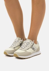 Zapatillas deportivas de color gris claro con parte superior de malla y cuero sintético, que presentan detalles en estampado de serpiente, texturas y cordones blancos.