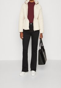 Veste matelassée crème avec capuche, haut bordeaux côtelé, jean noir évasé, baskets blanches et sac fourre-tout noir. Texture lisse dans l'ensemble.