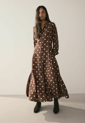 Brown polka dot dress with long sleeves, button closure, and flared skirt. Worn with dark brown ankle boots on a neutral background.