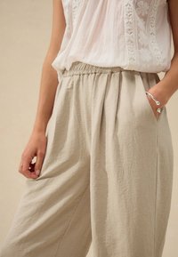 Kerged, beežid linased püksid elastse vöökohaga, volditud ees ja küljetaskutega. Sile tekstuur, lõdvestunud lõige, minimalistlik disain.