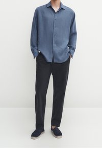 Lichtblauw overhem shirt van een zachte stof, gecombineerd met donkere broek en marineblauwe espadrilles. Het shirt heeft een klassieke kraag en lange mouwen.