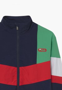 Farverig lynlåsjakke med marineblå, grønne, røde og hvide paneler med et Fila-logo. Letvægtsmateriale og høj krave design.