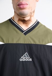 Svart och olivgrön träningsskjorta med V-ringning, har vita accenter och broderad Adidas-logotyp på framsidan. Mjuk textur.