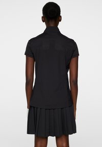 Svart kortärmad skjorta i slätt tyg, med krage och ryggsömnadsdetalj. Kombinerad med en plisserad svart kjol.