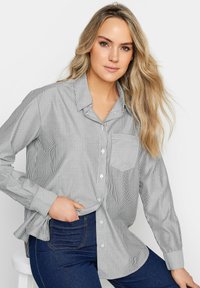 Chemise à rayures noir et blanc, dotée d'une poche poitrine et d'une coupe décontractée, associée à un jean bleu foncé. Tissu lisse.