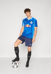 Maglia da calcio blu e turchese con maniche corte, con il logo Red Bull. Abbinata a pantaloni corti blu navy, calzettoni neri e scarpini. Incluso il pallone.