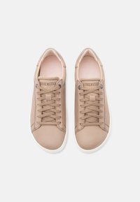 Ζευγάρι μπεζ αθλητικών παπουτσιών Birkenstock με κορδόνια και λευκές σόλες, φωτογραφημένα από πάνω σε ανοιχτό φόντο.