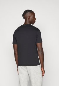 Μαύρο βαμβακερό μπλουζάκι με στρογγυλή λαιμόκοψη και κοντά μανίκια, με απαλό ύφασμα και άνετη εφαρμογή. Φορεμένο με γκρι φόρμα παντελόνι.