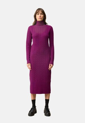 Vestido largo y ajustado de cuello alto en un vibrante color púrpura con textura de punto trenzado, puños y dobladillo acanalados, combinado con zapatos y calcetines negros.