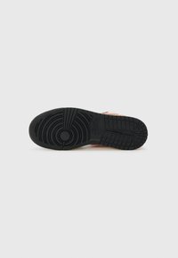 Suola di sneaker in gomma nera con motivo di battistrada circolare e sezioni di presa testurizzate. Presenta accenti di colore arancione e bianco sui lati.