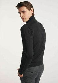 Czarny sweter z wysokim kołnierzem, o dopasowanym kroju i ściągaczach na rękawach. Noszony z szarymi spodniami w kant z guzikiem na tylnej kieszeni.