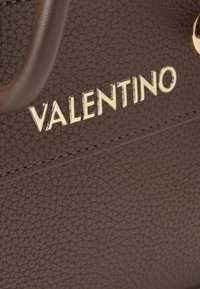 Smeđi kožni ručni kovčežić s teksturom, s zlatnim logotipom "VALENTINO" i akcentima od šivanja. Uključuje glatke ručke i metalne detalje.